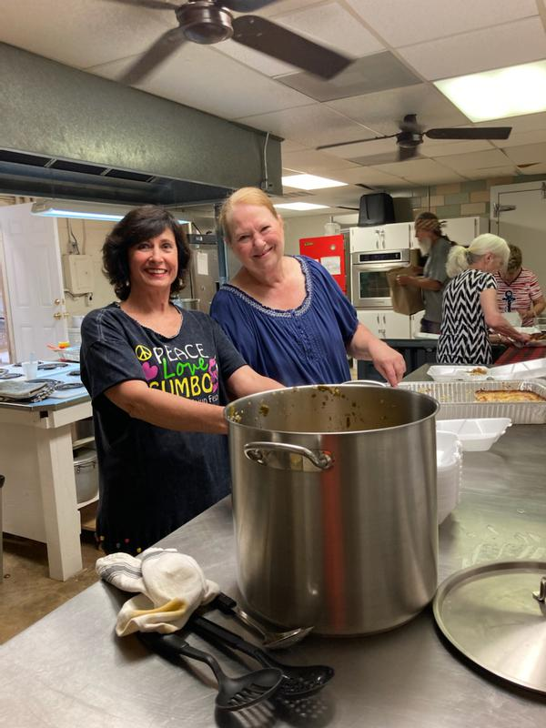 Gumbo Cook-Off volunteers smiling beside a large gumbo pot in the kitchen